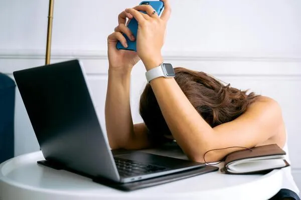 A woman rests her head in her hands while lying on her laptop, conveying a sense of stress or fatigue.