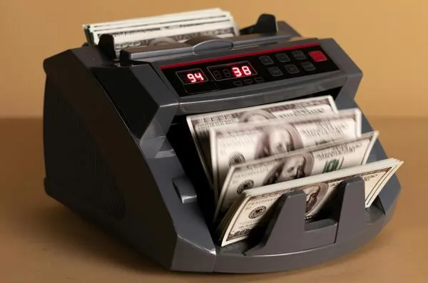 A cash counting machine in black and gray, set against a brown background.