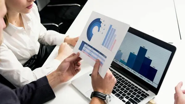 Business professionals analyzing market trend graphs on a laptop during a meeting.