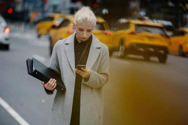 A woman in a coat is intently looking at her phone, possibly checking messages or browsing online content.