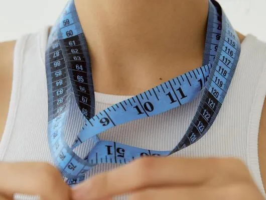 A woman holds a measuring tape around her neck, emphasizing the importance of sizing charts for online fashion shopping.