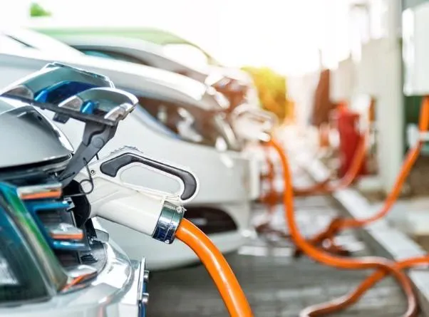 ComEd representative speaking at a press conference with EV chargers in the background, announcing a major rebate program.