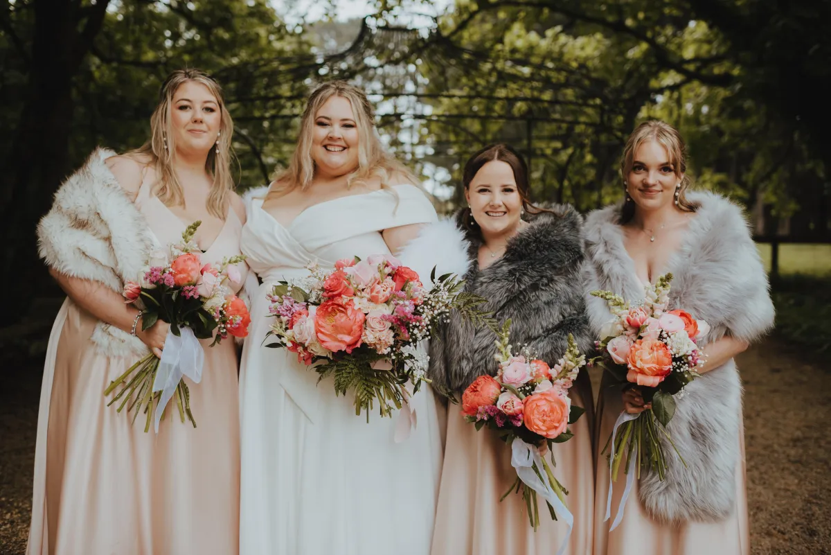 bridal party posing with the bride and their pink and orange florals