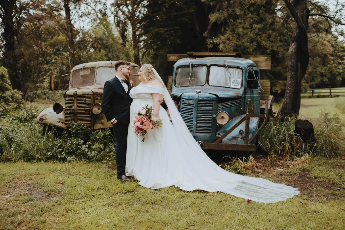 newlyweds posing with old rusty cars