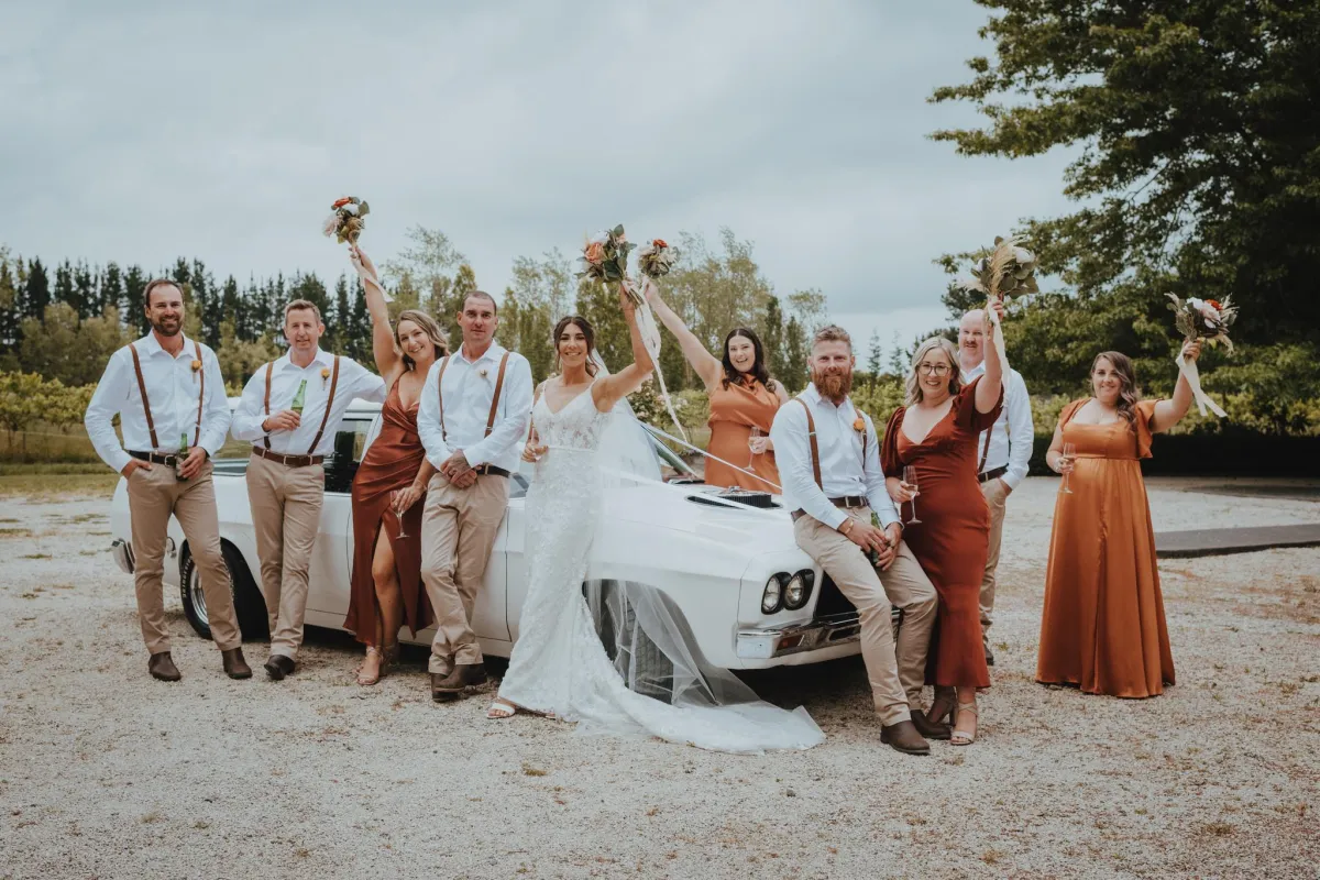 Bridal Party Group Photograph infront of car with everyone smiling and bridesmaids holding up bouquets