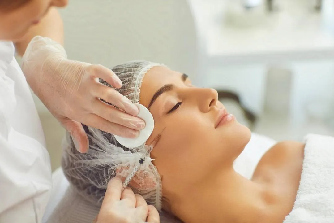 Professional administering dermal fillers to woman's face in clinical setting for anti-aging cosmetic treatment.
