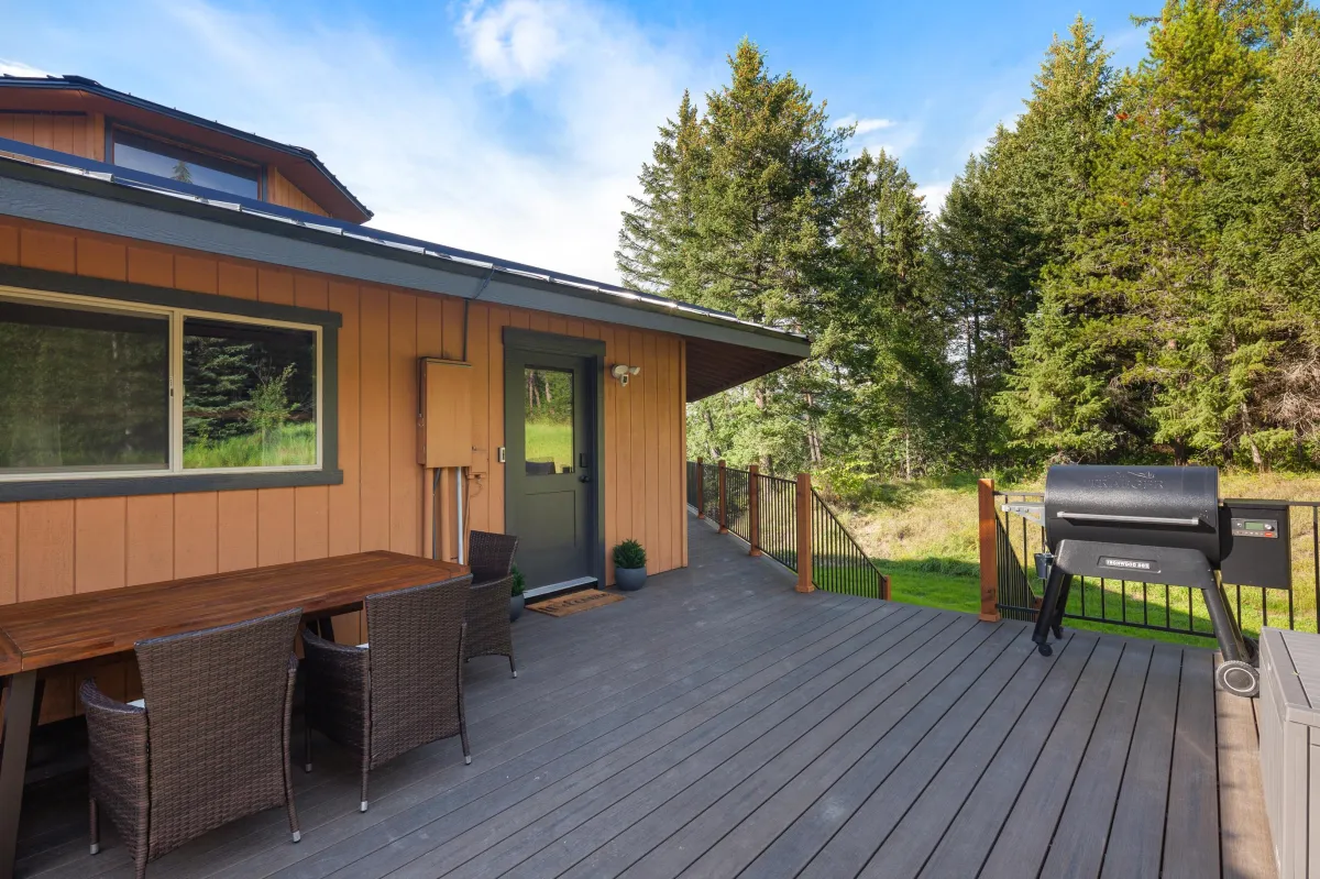 Welcoming front entrance and deck at Glacier Gateway Lodge in Montana, complete with dining table, chairs, and a Traeger pellet grill. Built for entertaining from the moment you arrive, the deck wraps around to a covered seating area with breathtaking views of the Flathead River and surrounding mountains.