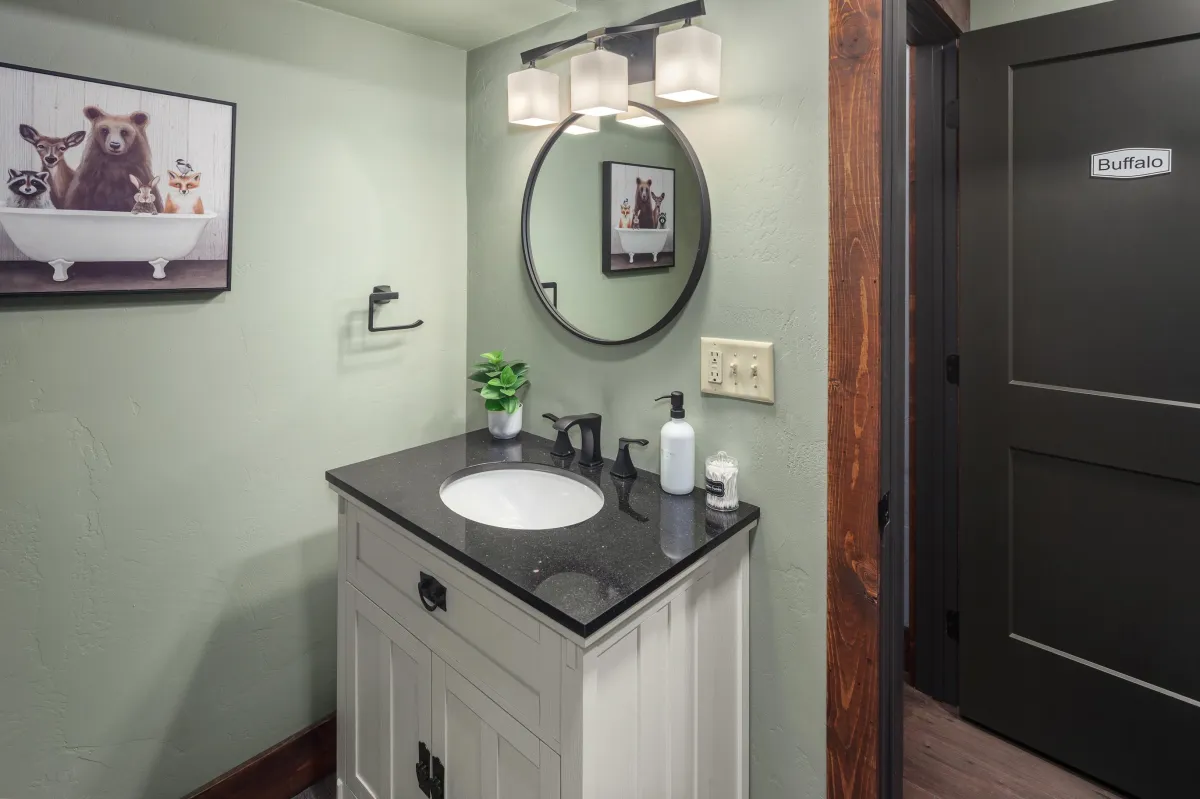 Elegant bathroom featuring a granite vanity, circular mirror, and stylish lighting. Perfect for refreshing after exploring Montana’s Rocky Mountains or Glacier National Park.