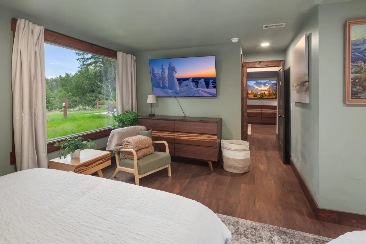 The Buffalo room, featuring two king beds and lower-level views of the wooded lot, Flathead River, and Rocky Mountains. A cozy, Western-themed retreat with sitting area and Smart TV in this luxury Montana lodge near Glacier National Park.