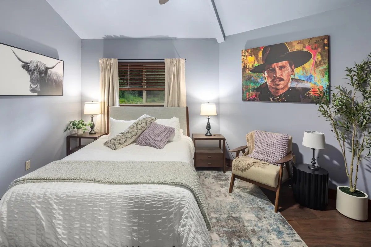 Step into the Holliday room, one of six themed bedrooms, featuring a queen bed, tasteful Western decor, and a striking Val Kilmer as Doc Holliday painting. A serene retreat for peaceful nights in Big Sky Country.