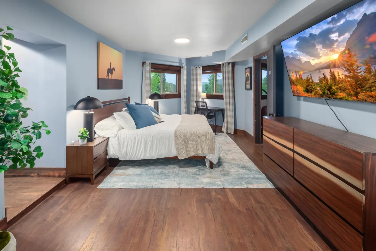 Sunset King Bedroom features a plush king bed, Western-inspired art, and large windows overlooking th peaceful wooded lot. One of six themed bedrooms, it offers a peaceful retreat after exploring Glacier National Park or Montana’s great outdoors.