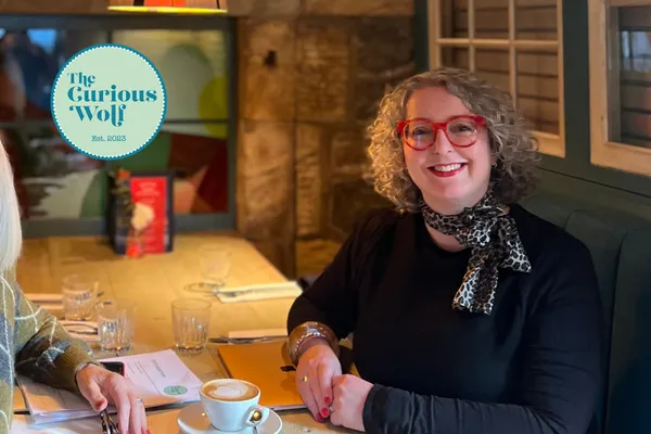 Suzanne Ulph of The Curious Wolf sitting at a wooden table and smiling at the camera.