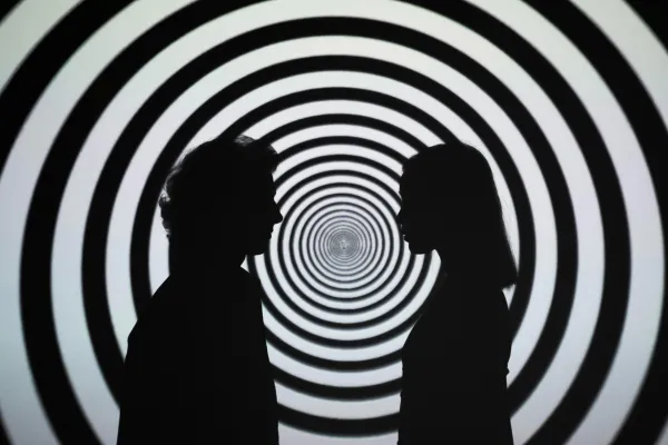 A silhouette of a man and a woman with a hypnotic spiral behind them to illustrate hypnosis to laymen