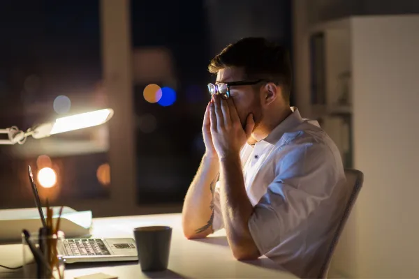 Exhausted real estate agent at desk surrounded by papers and devices representing hustle culture burnout