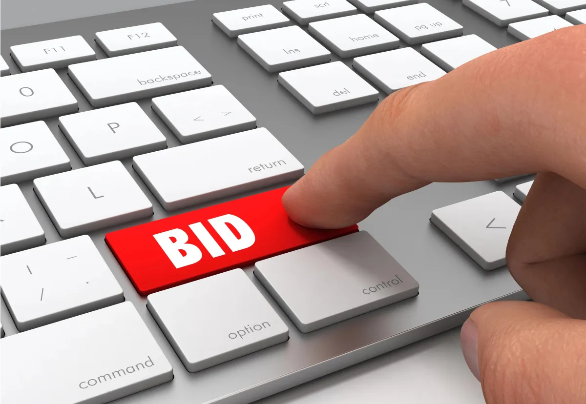 A close-up of a finger poised to press a bright red key on a silver computer keyboard. The key is labeled with the word "BID" in bold, white capital letters.