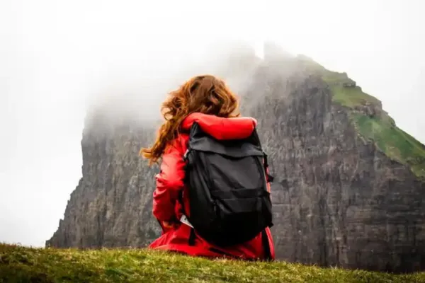 A woman sitting on a mountain with a backpack on her back