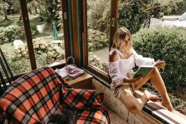 A woman reading a book sitting on a windowsill