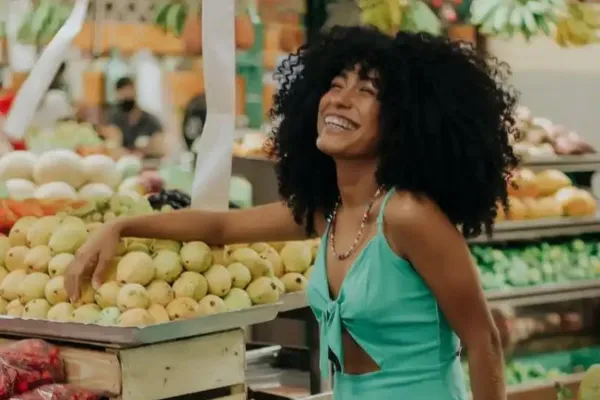 A woman laughing by some vegetables in a supermarket