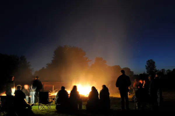 โGroup of bikers laughing around a campfire with tents behind them.โ