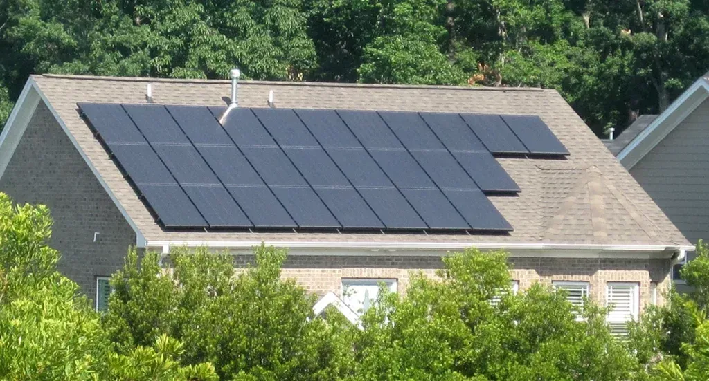 A charming brick home in Salem, UT, with a well-installed array of dark solar panels covering the roof, surrounded by lush green trees and neighboring houses, showcasing a blend of modern renewable energy and natural beauty.