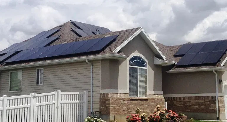A luxurious Alpine, UT home with solar panels and a solar fan on the roof, illuminated by a vibrant sunset, surrounded by scenic hills, symbolizing innovative savings.