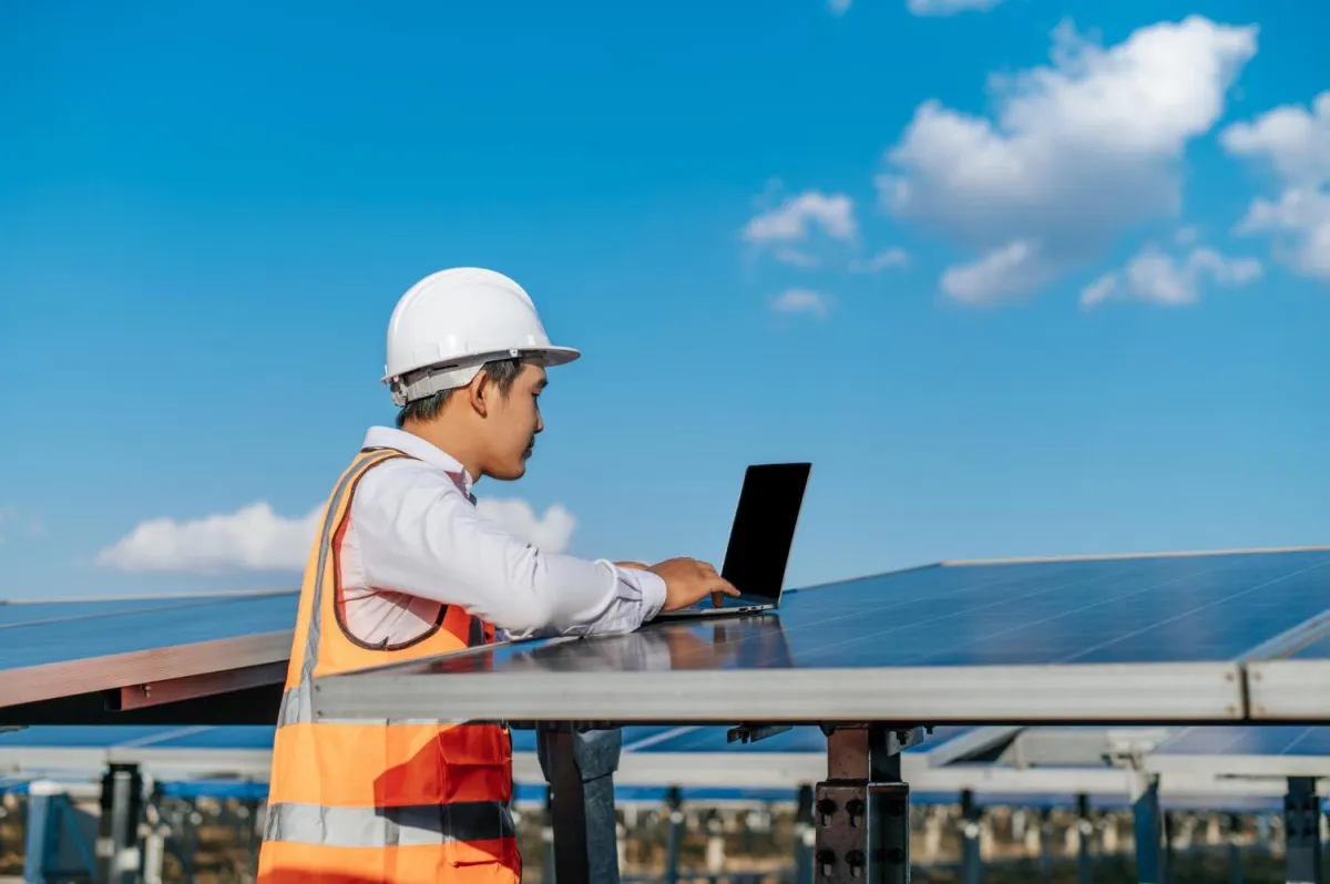 A commercial solar contractor stands with his laptop on a solar panel in Dubai