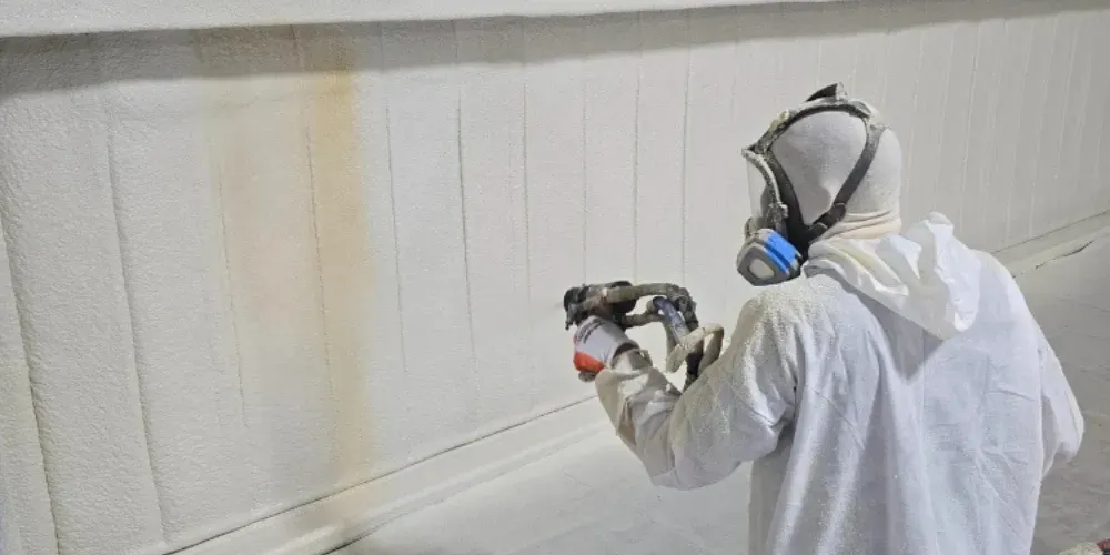 Technician applying open cell spray foam insulation to wall framing for superior R-value and energy efficiency