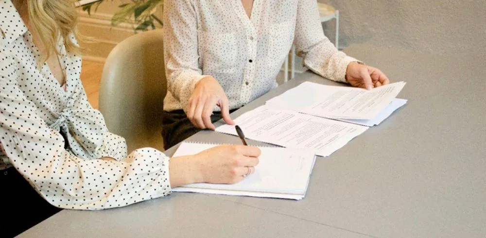 Two women reviewing documents and completing paperwork side by side