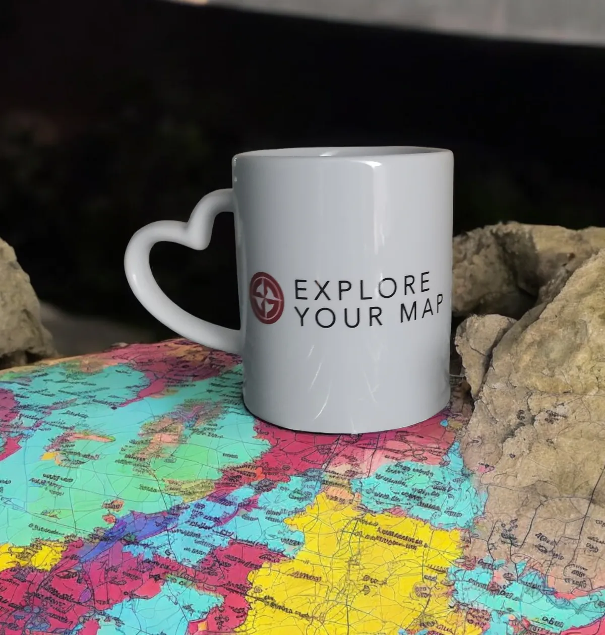 A white mug with a heart-shaped handle and the text "Explore Your Map," placed on a colourful world map.