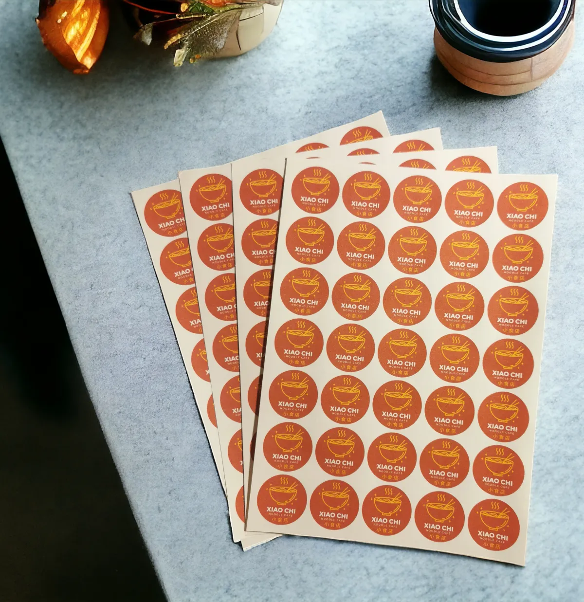 Four sheets of circular red stickers with a logo and text, placed on a grey surface.