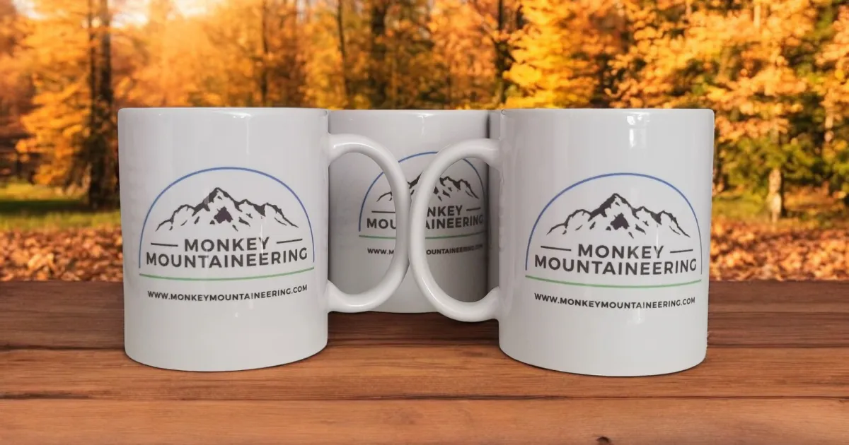 Three white mugs with the words Monkey Mountaineering on the front with a blue half circle outline over the top.