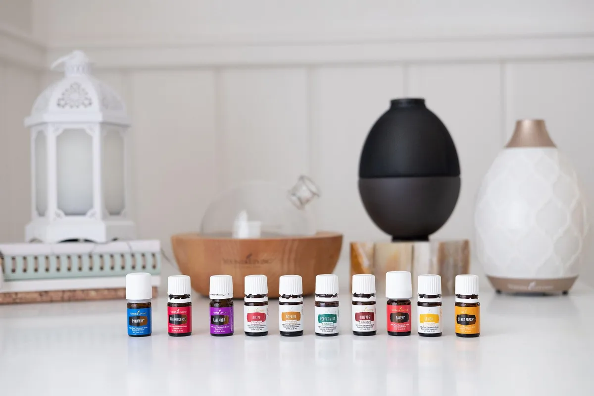 image of 10 different essential oil diffuser scents from young living lined in a row sitting in front of a white and a black oil diffuser on a white countop background