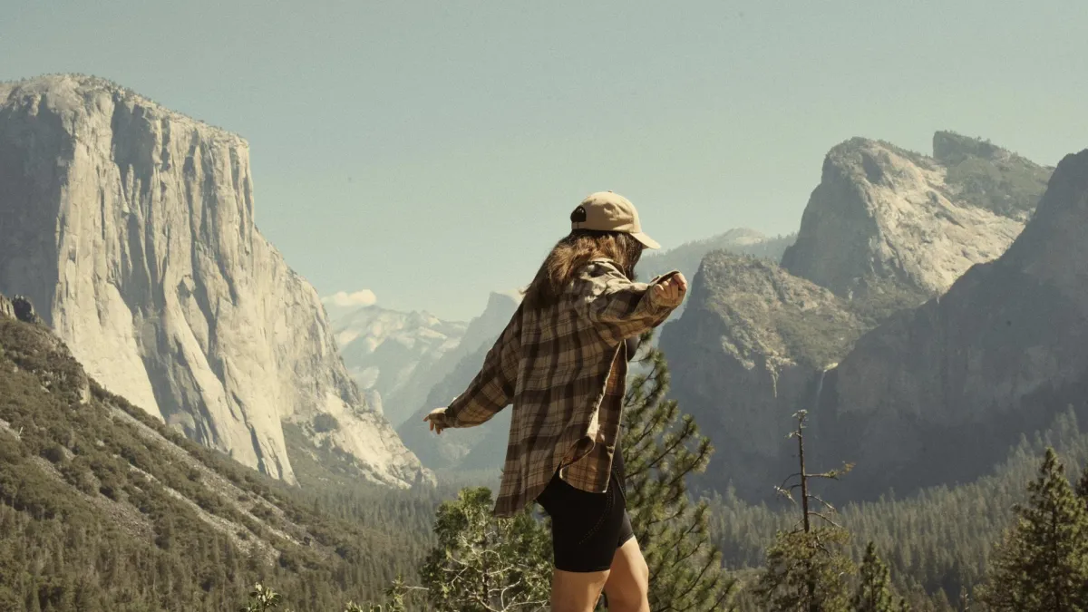 Professional woman balancing on a rocky edge in the mountains, symbolizing freedom and empowerment after leaving a toxic relationship, with expansive peaks in the distance.