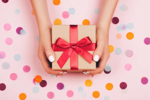 ladies hands holding a gift with pink ribbon around it 