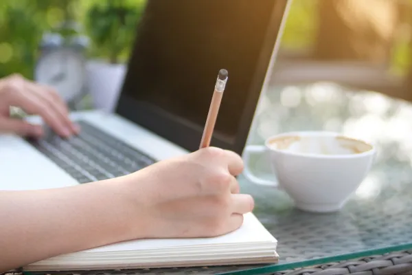 laptop open with a cup of coffee and a person holding a pencil