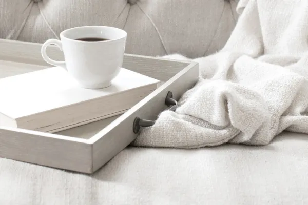 tray with a book and coffee mug on top resting on a bed