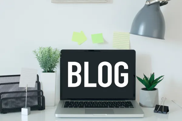 laptop on a desk with pot plants and a desklamp and the word blog on the screen of laptop 