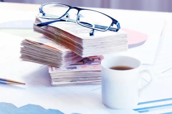 piles of money notes with a pair of glasses on the top and a cup of coffee next to it