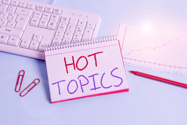 A white keyboard and a graph with a notepad with the words hot topics written on it