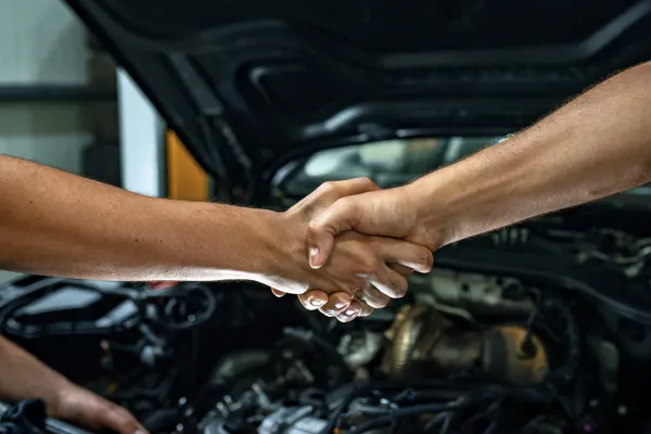 Two people shaking hands in front of a car with the hood open