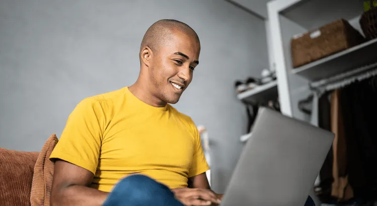 Person holding a credit card and pen, reviewing their credit score on a document with a laptop in the background.