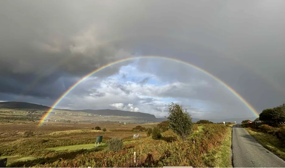 rainbow over an open field with a winding road symbolizing hope, nervous system safety, and the shift from pain as danger to pain as protection