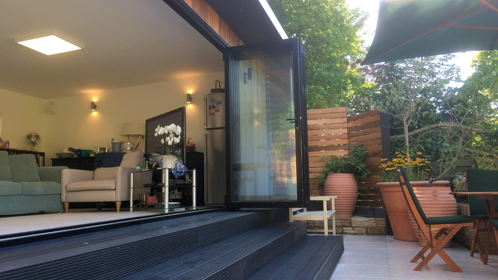 Modern garden room opening onto a porcelain tile terrace in a design-led Carshalton Beeches garden by EarthCare Gardens