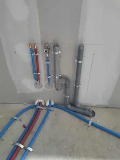 Tuyauterie murale en PVC rouge bleu gris, raccords et vannes pour plomberie neuve.