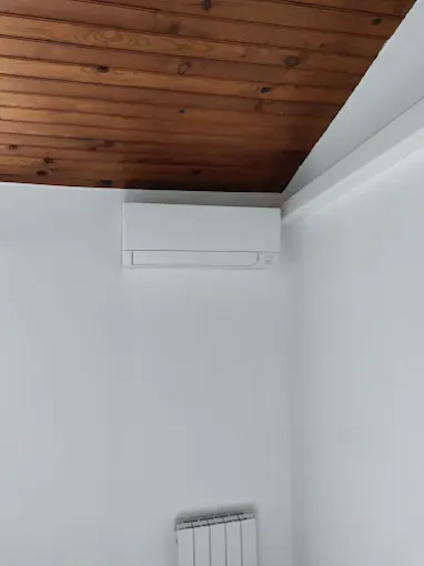 Climatiseur mural blanc installé au plafond en bois dans une pièce aux murs blancs avec moulures.