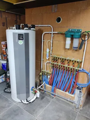 Chauffe-eau électrique vertical blanc avec tuyaux et raccords dans un local technique.