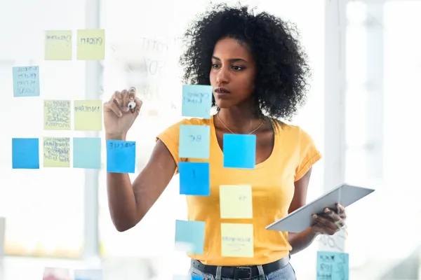Shot of young businesswoman using a digital tablet while brainstorming with notes on a glass wall in an office