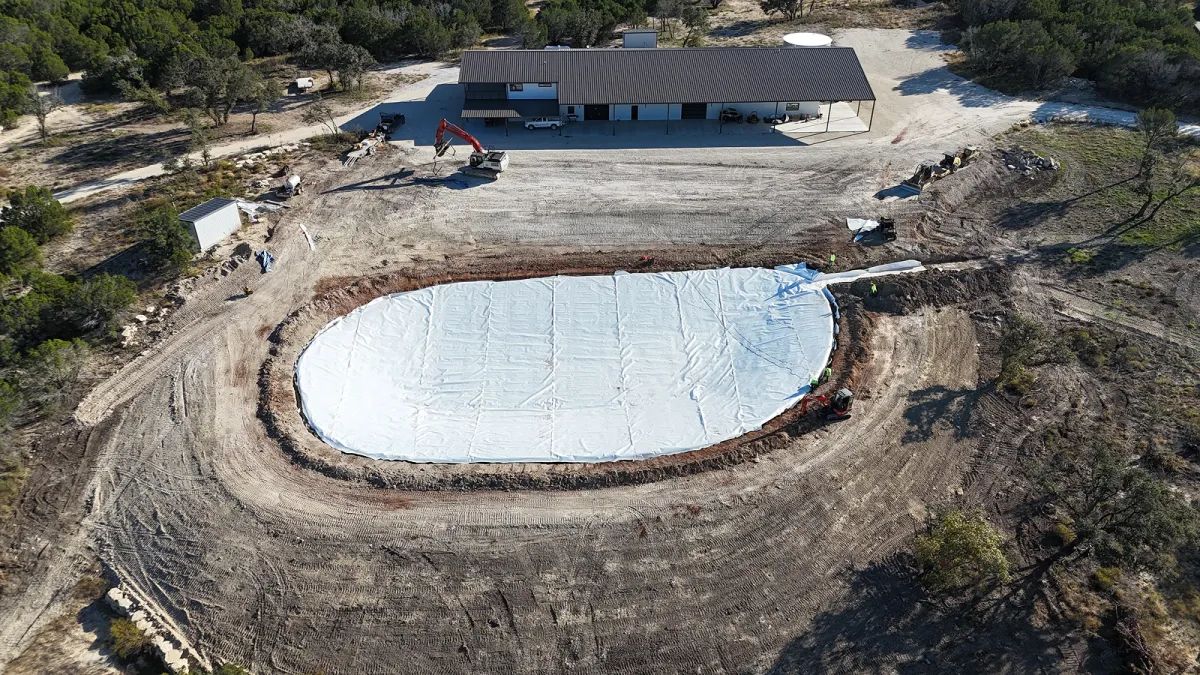 A ranch pond with a newly installed HDPE liner, surrounded by livestock and open land, showcasing durability for agricultural use.