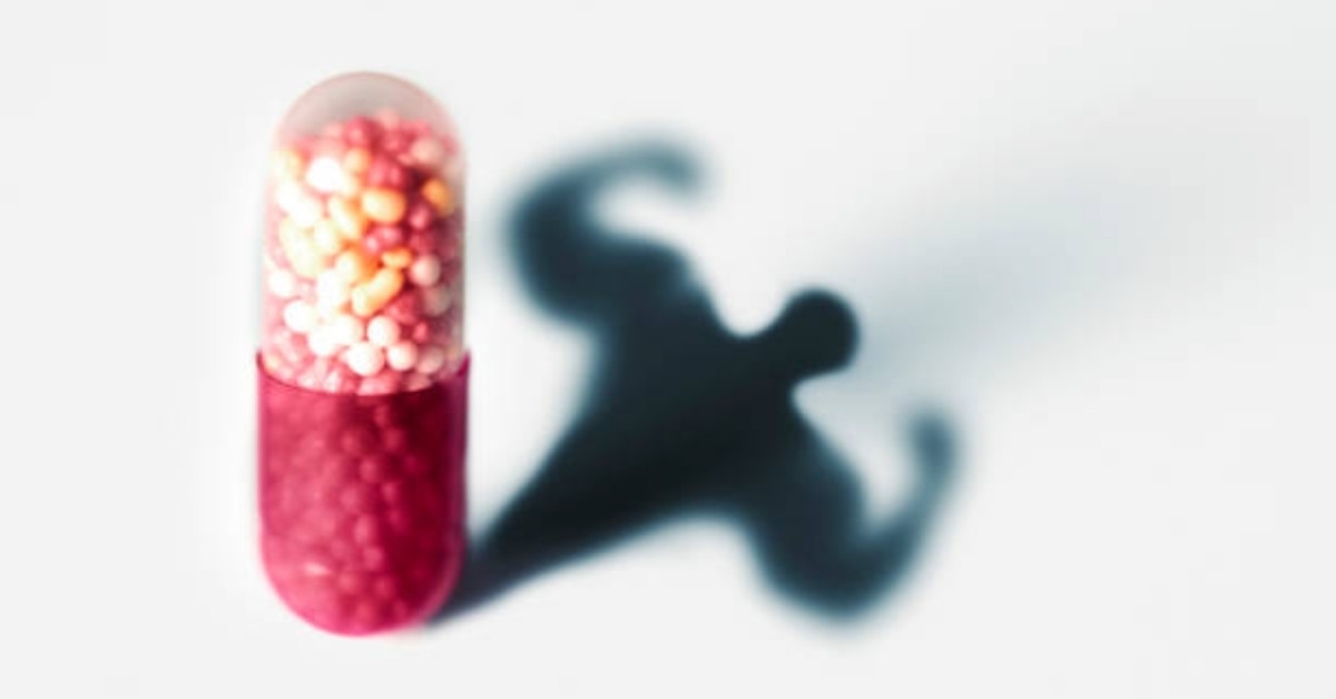 A red and white capsule pill casts a shadow shaped like a muscular bodybuilder, symbolizing the concept of steroid use and performance enhancement in sports.