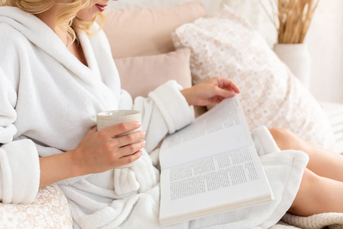 woman in bathrobe reading and drinking tea